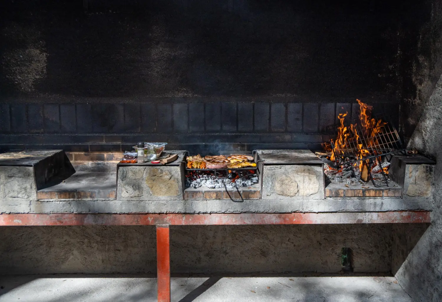 Exemplo de churrasqueira de bloco de concreto simples Exemplo de churrasqueira de bloco de concreto simples com fogo aceso e carne sendo assada na grelha