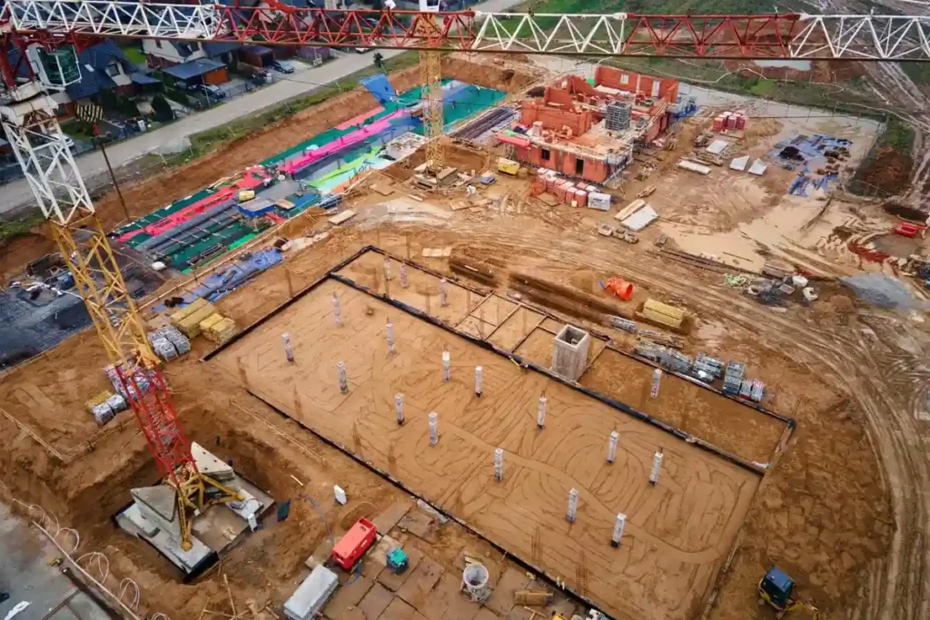 Vista aérea de um canteiro de obras amplo com guindastes, casas em construção e área de armação de fundação